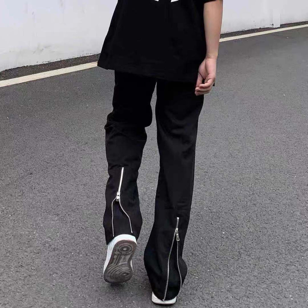 Person wearing black pants with zippers on a gray pavement.