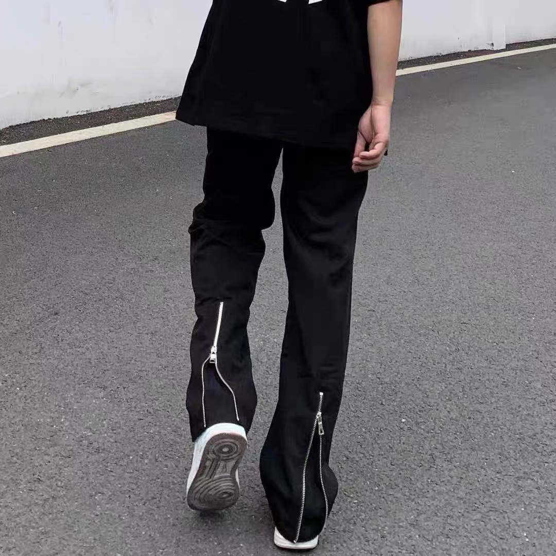 Person wearing black pants with zippers on a gray pavement.