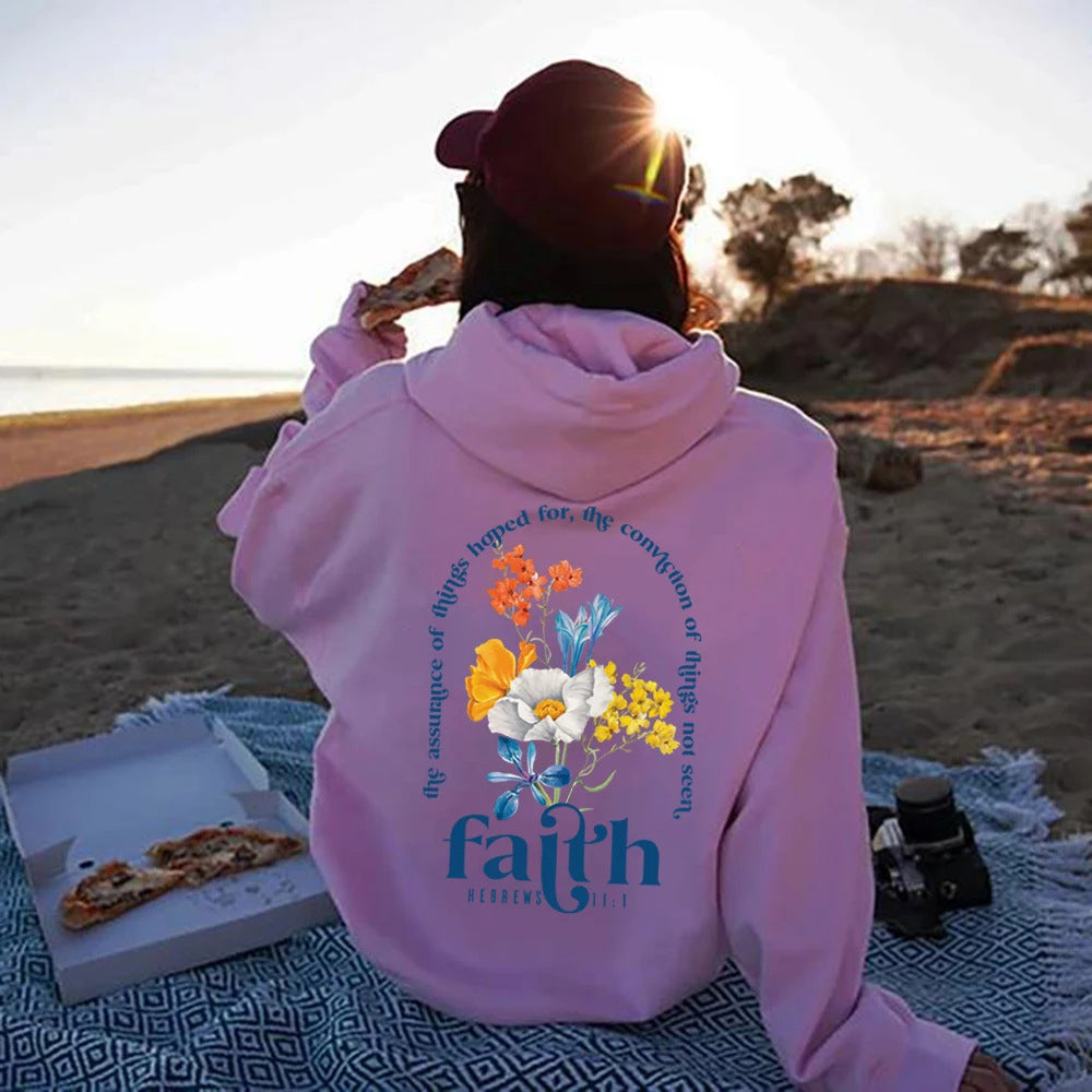 Person wearing a pink hoodie with floral design and 'faith' text on a beach
