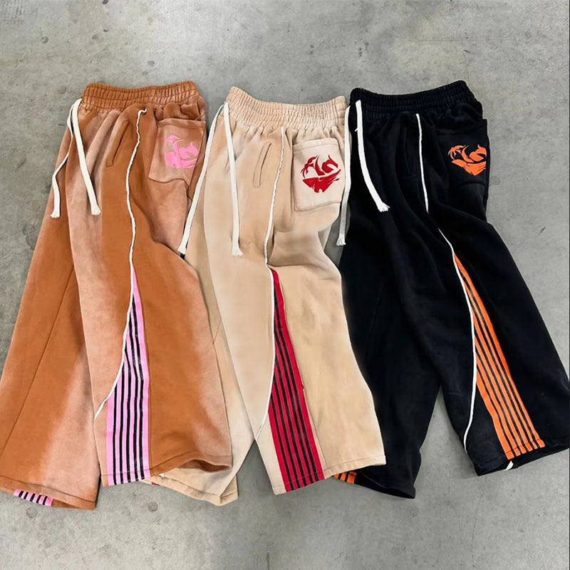 Three pairs of colorful sweatpants on a gray concrete surface