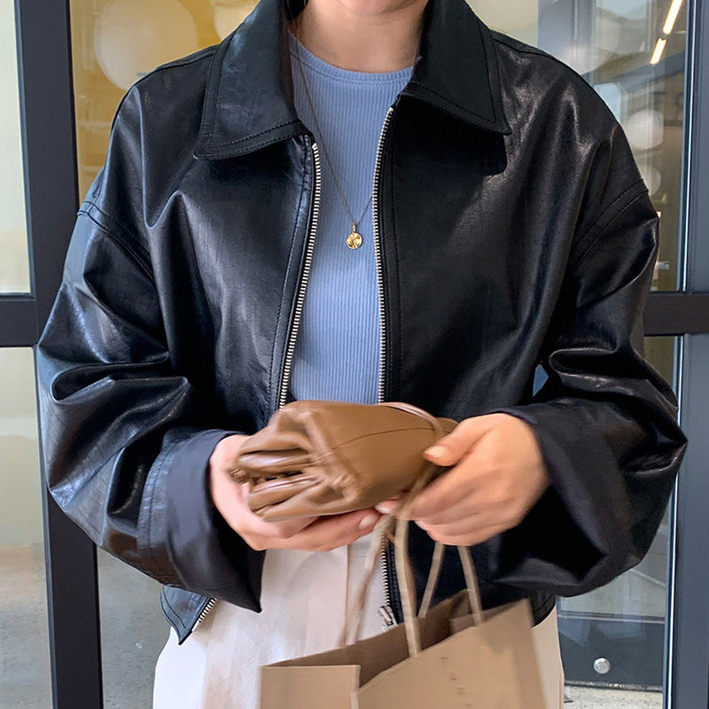 Person wearing a black leather jacket holding a brown leather wallet and a paper bag.